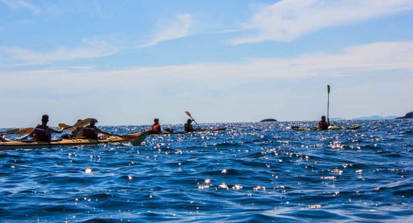 a group of outward bound gap year students paddle kayaks on a blue lake under blue skies in minnesota